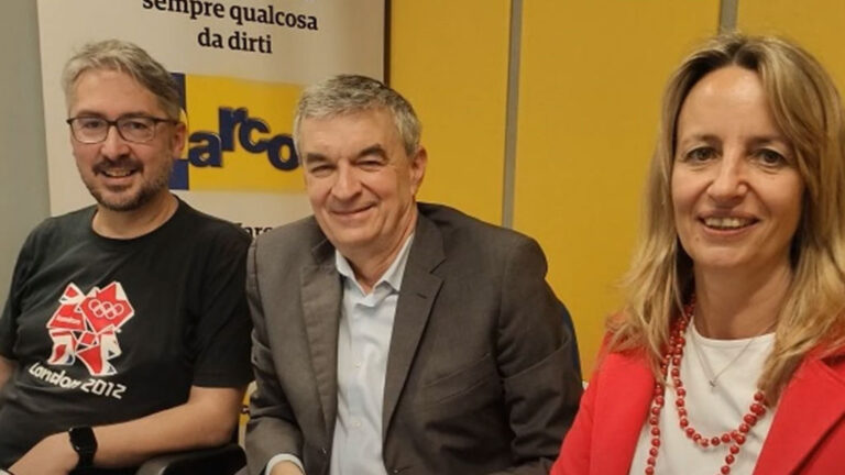 Persone sorridenti in ufficio con logo aziendale.
